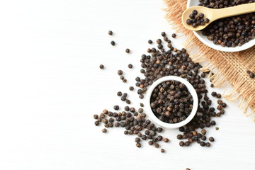 Black peppercorns in bowls on white wooden background