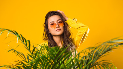 Naklejka premium a girl of Asian appearance in yellow glasses, yellow clothes, on a yellow background, looking at the camera, in the foreground there is a large flower