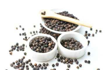 Black peppercorns in bowls on white wooden background
