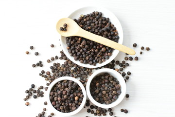 Black peppercorns in bowls on white wooden background