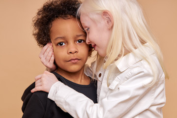 sensitive albino child girl hug african boy isolated in studio. adorable girl with white hair has tender feelings for the boy