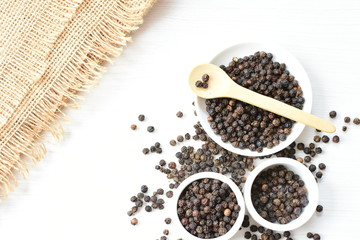 Black peppercorns in bowls on white wooden background