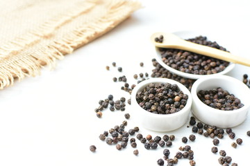 Black peppercorns in bowls on white wooden background