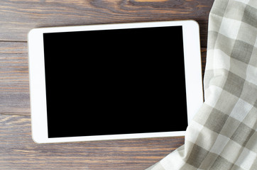 A tablet computer and a tablecloth on a brown wooden background. Copy space. Concept of cooking recipes
