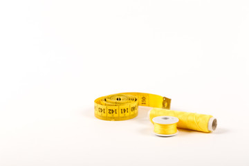 A centimeter tape and two spools of yellow thread on a white background in a minimalistic style with a place for text. Items for needlework, embroidery, sewing and cutting clothes.