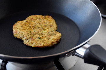 Chicken fillet fried in a pan. Chop is prepared with herbs and spices. Fresh hot roasted meat. Pan is on gas plate. Closeup black background.