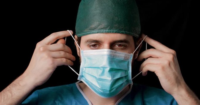 Medico si mette correttamente la mascherina chirurgica, sfondo nero.