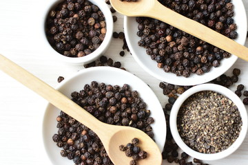 Black peppercorns in bowls on white wooden background