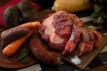 Osobuco carne cruda y chorizo mas ingredientes para preparar un puchero o guiso sobre tabla de madera 
