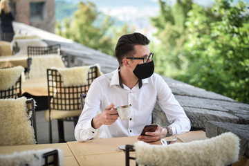 Young fashion Businessman with face mask drinking espresso coffee in the city cafe during lunch time and working on smartphone