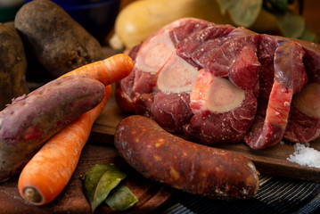 Osobuco carne cruda y chorizo mas ingredientes para preparar un puchero o guiso sobre tabla de madera 