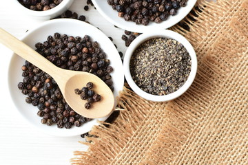 Black peppercorns in bowls on white wooden background