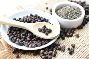 Black peppercorns in bowls on white wooden background