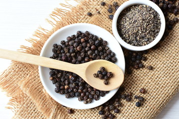 Black peppercorns in bowls on white wooden background