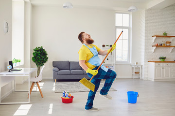 Funny fat man with a beard in an apron dancing cleans the room in the house. - Powered by Adobe