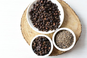 Black peppercorns in bowls on white wooden background