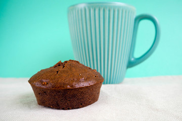 gluten-free brown chocolate muffin made from rice flour and cocoa on a light table against a large blue mug. breakfast