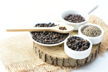 Black peppercorns in bowls on white wooden background