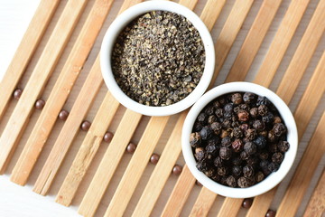 Black peppercorns in bowls on white wooden background