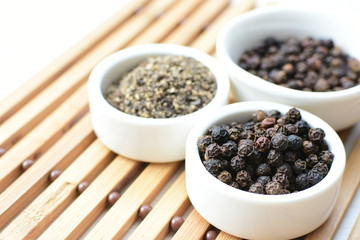 Black peppercorns in bowls on white wooden background