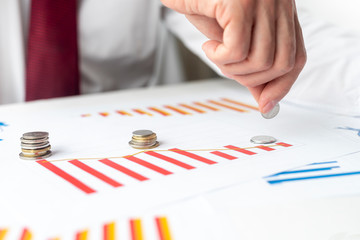 stacks of coins like diagram on red chart graph of worsening economic performance and hand put coin...