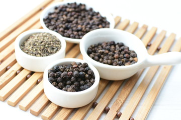 Black peppercorns in bowls on white wooden background