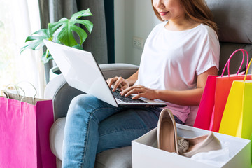 Young woman using laptop computer sitting on sofa with her fashion items. Online shopping, e-commerce, internet banking, payment of financial management, work at home concept