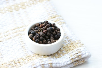 Black peppercorns in bowls on white wooden background