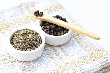 Black peppercorns in bowls on white wooden background