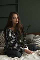 girl sitting on a bed in a plaid shirt holding a flower between her legs