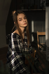 Fototapeta na wymiar the girl sits on a chair in a plaid shirt, put her hands on the back of the chair, the ray of the sonde falls on her face
