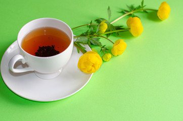 A Cup of black tea and yellow flowers of Trollius europaeus on a green background. Evening and...