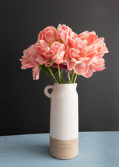 Bouquet of coral fragrant peonies in a white ceramic pot.