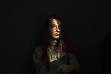 portrait of a girl against a dark background, the light from the window falls on the girl’s face, I create shadow stripes on the blinds