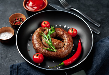 grilled spiral sausage with spices in a pan on a stone background 