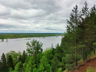 wooded slope near the river against a gloomy sky with clouds