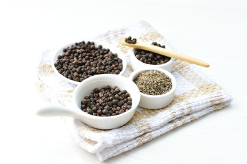 Whole and ground black peppercorns on white wooden background