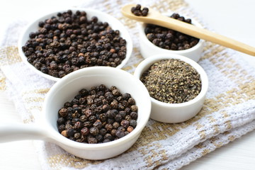 Whole and ground black peppercorns on white wooden background