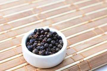 Whole and ground black peppercorns on white wooden background