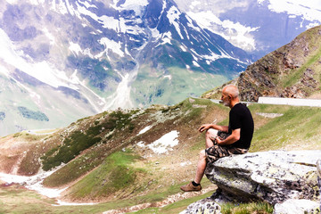 Naklejka premium Man on top of mountain. Conceptual design. An elderly man sits on top of a mountain. Active holiday in retirement. Time is one with itself. Mountain landscape in the Alps.