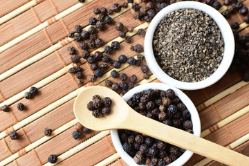 Whole and ground black peppercorns on white wooden background