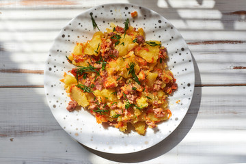 Baked potatoes with minced meat, onions and carrots baked on a plate on a light wooden background.
