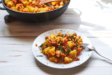 Baked potatoes with minced meat, onions and carrots baked on a plate on a light wooden background.