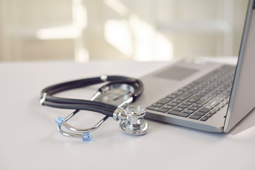 Doctor online. A stethoscope is on a white table with a laptop in blur at the hospital office.