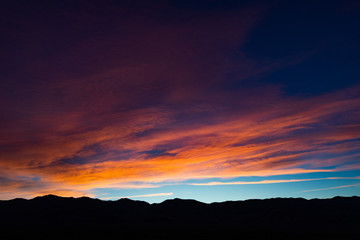 A stunning sunset or sunrise scene of silhouette mountain peaks and purple ridges with the twilight background, the blue sky and the pink-yellow skyline