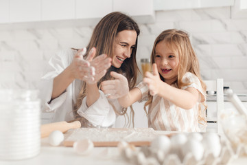 Obraz na płótnie Canvas Happy mother with her daughter preparing dough and having fun in kitchen. Cooking homemade food.