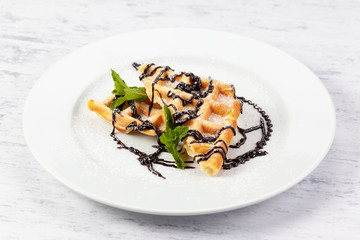 Belgian waffles in powdered sugar with chocolate syrup and mint.