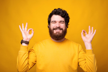 Smiling bearded man is trying to get calm on yellow.