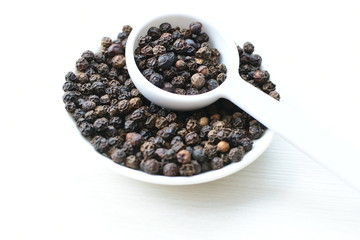Whole and ground black peppercorns on white wooden background