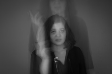 artistically blurred photo, a girl stands on a gray background in her teeth holds a cigarette